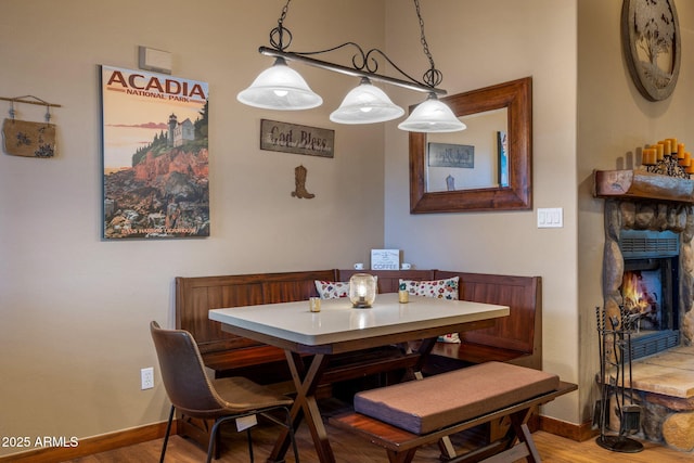 dining space featuring breakfast area, a stone fireplace, baseboards, and wood finished floors