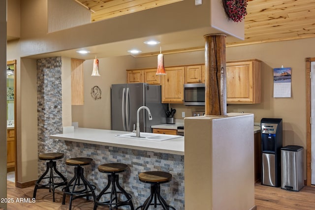 kitchen with stainless steel appliances, light wood-type flooring, light countertops, and a breakfast bar area