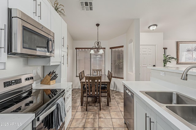 kitchen featuring light countertops, a sink, a notable chandelier, decorative light fixtures, and stainless steel appliances