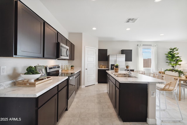 kitchen featuring stainless steel appliances, dark brown cabinets, sink, and a kitchen island with sink