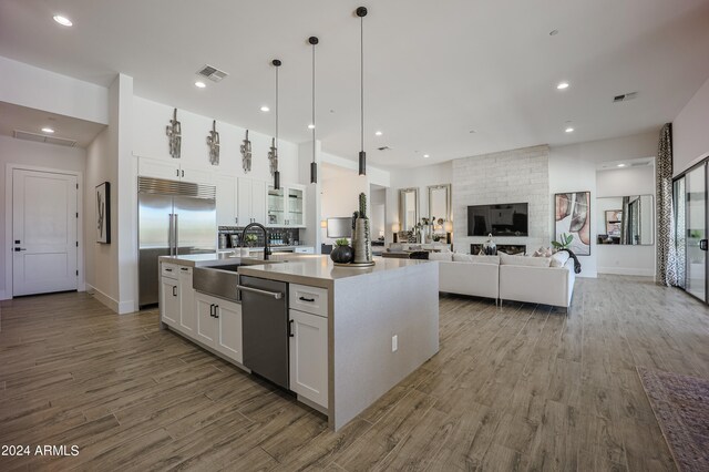 kitchen featuring white cabinets, an island with sink, appliances with stainless steel finishes, hardwood / wood-style floors, and sink