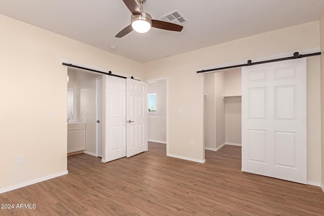 unfurnished bedroom featuring a barn door, ceiling fan, hardwood / wood-style floors, and ensuite bathroom