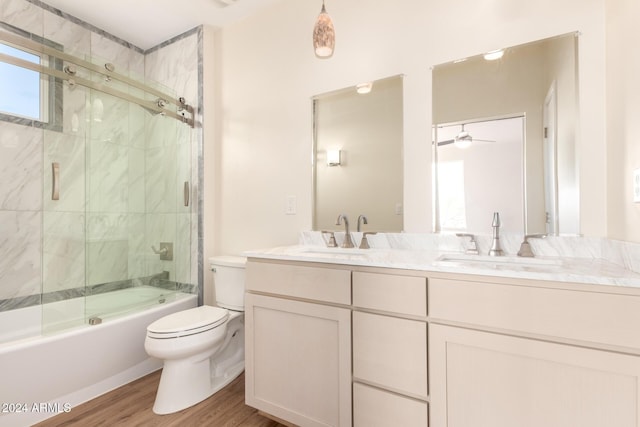 full bathroom with bath / shower combo with glass door, vanity, ceiling fan, hardwood / wood-style floors, and toilet