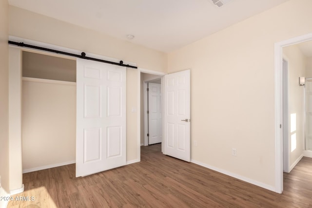 unfurnished bedroom with a barn door, a closet, and hardwood / wood-style floors