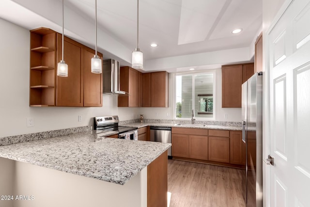 kitchen with sink, wall chimney range hood, kitchen peninsula, appliances with stainless steel finishes, and light wood-type flooring