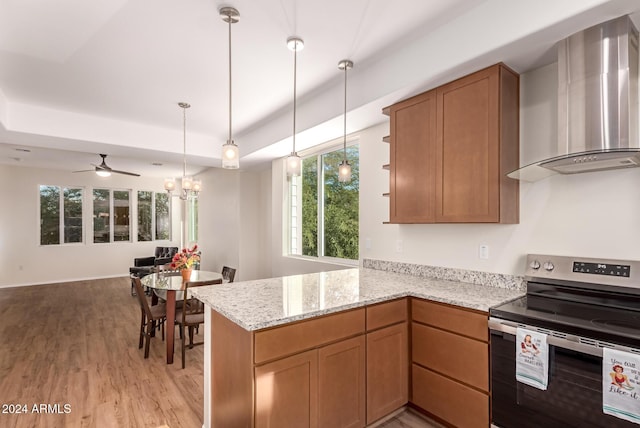 kitchen featuring wall chimney range hood, kitchen peninsula, electric stove, ceiling fan with notable chandelier, and light wood-type flooring