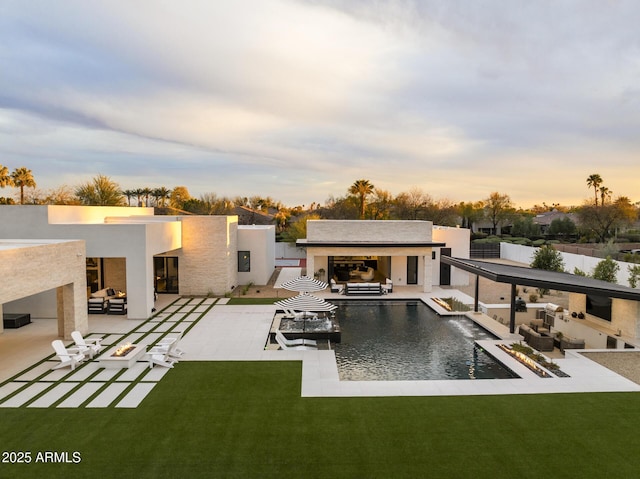 back of property at dusk with an outdoor living space with a fireplace, stucco siding, an outdoor pool, a lawn, and a patio