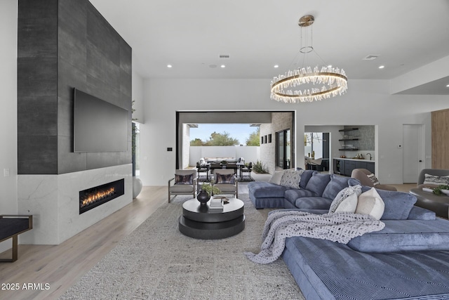 living room featuring light wood-style floors, a large fireplace, recessed lighting, and an inviting chandelier