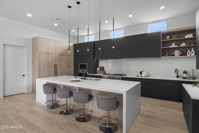 kitchen with a sink, dark cabinetry, modern cabinets, and a center island with sink