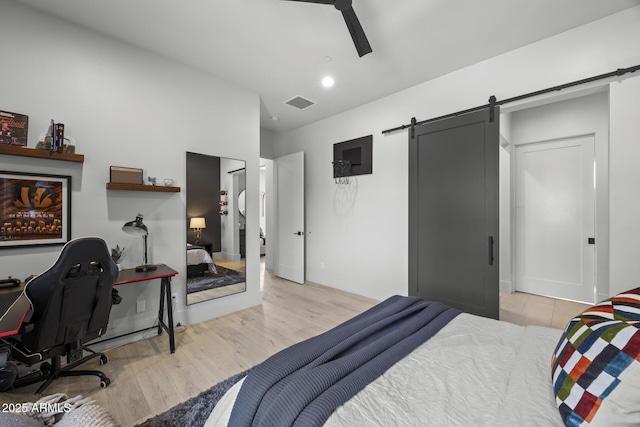 bedroom with a barn door, light wood finished floors, a ceiling fan, baseboards, and visible vents