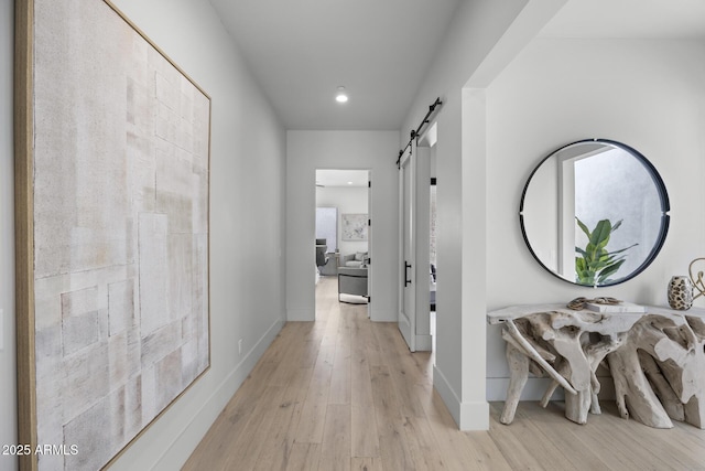 corridor with recessed lighting, baseboards, light wood-type flooring, and a barn door