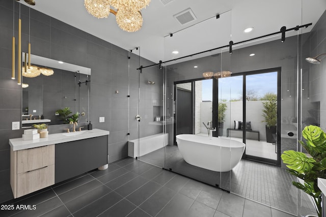 full bathroom with an inviting chandelier, vanity, tile walls, tile patterned floors, and a shower stall