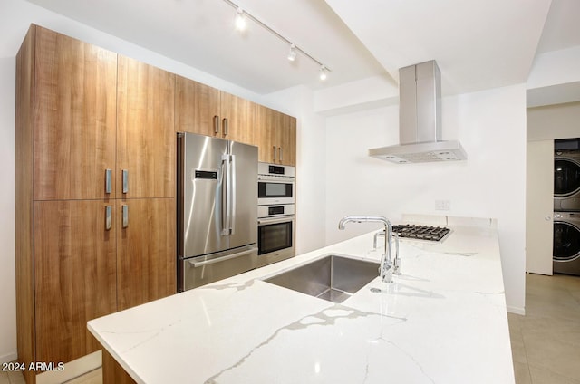 kitchen featuring light stone countertops, sink, ventilation hood, stacked washer and clothes dryer, and appliances with stainless steel finishes