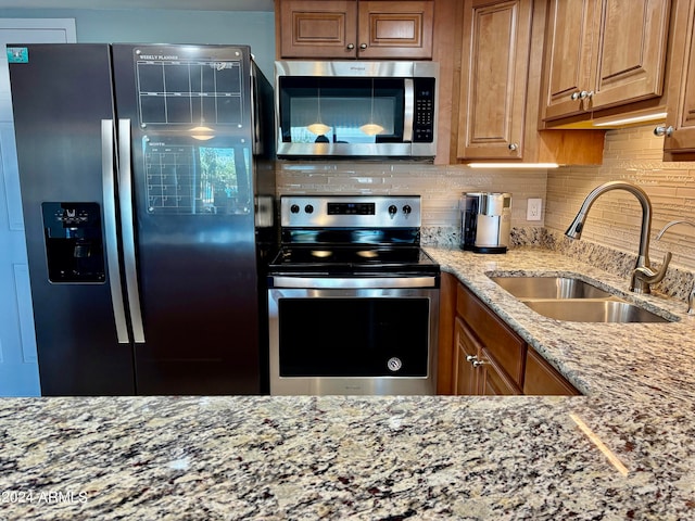 kitchen with appliances with stainless steel finishes, backsplash, light stone counters, and sink