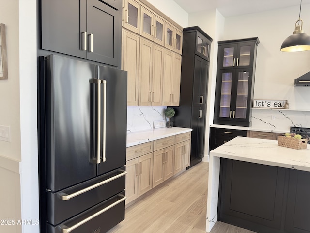 kitchen with high end refrigerator, light wood-style floors, backsplash, and light stone countertops