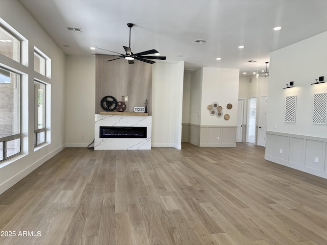 unfurnished living room featuring a high end fireplace, a ceiling fan, light wood-style flooring, recessed lighting, and a chandelier