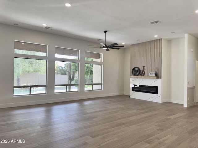 unfurnished living room featuring plenty of natural light, a ceiling fan, baseboards, a high end fireplace, and recessed lighting