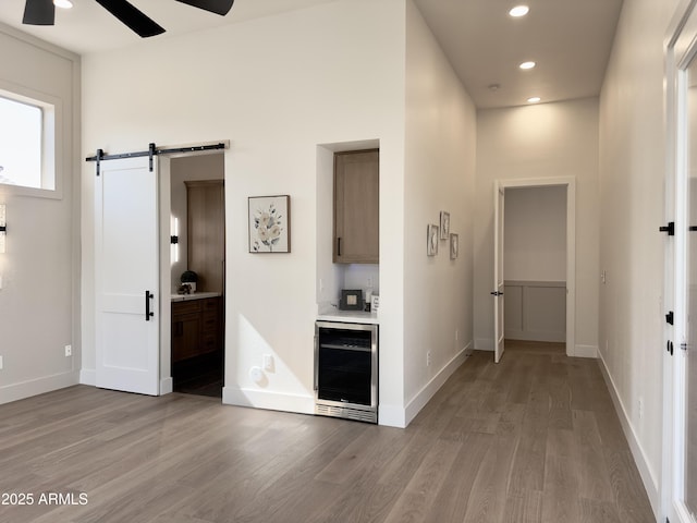 hallway featuring beverage cooler, a barn door, light wood-style floors, recessed lighting, and baseboards