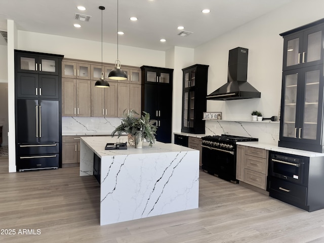 kitchen featuring built in refrigerator, wall chimney range hood, range with gas stovetop, a kitchen island, and tasteful backsplash
