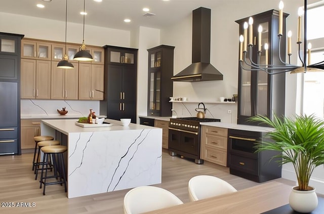 kitchen with high quality appliances, wall chimney exhaust hood, light wood-type flooring, recessed lighting, and a kitchen island