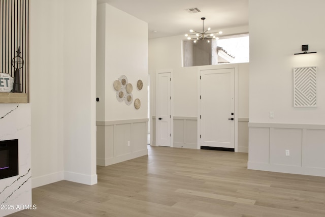foyer entrance featuring a chandelier, light wood-style floors, a decorative wall, wainscoting, and a high end fireplace