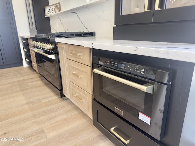 kitchen with stainless steel range with gas stovetop, light countertops, light wood finished floors, wall oven, and open shelves