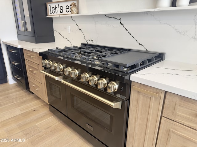 kitchen with double oven range, light wood finished floors, light countertops, light brown cabinets, and decorative backsplash