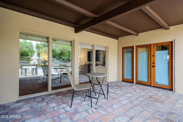 sunroom featuring beam ceiling and french doors