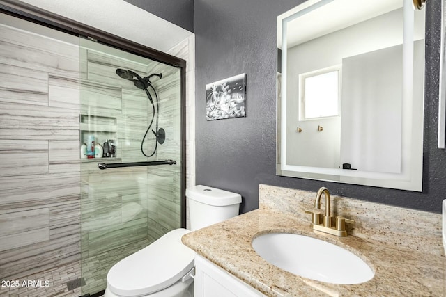 bathroom featuring a stall shower, toilet, vanity, and a textured wall