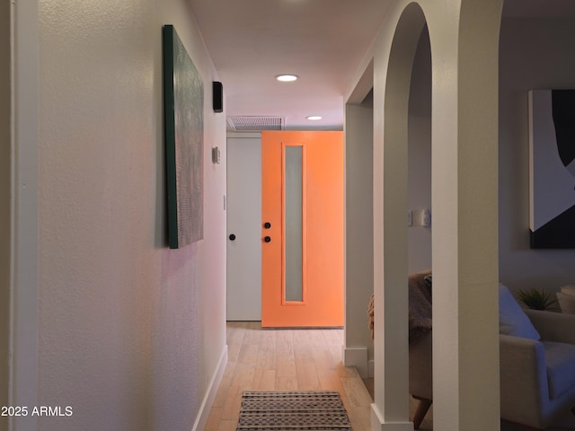 corridor with light wood finished floors, visible vents, arched walkways, and recessed lighting