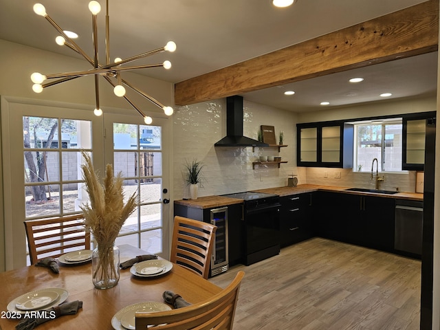 kitchen featuring electric range, a sink, light wood finished floors, dark cabinets, and wall chimney exhaust hood