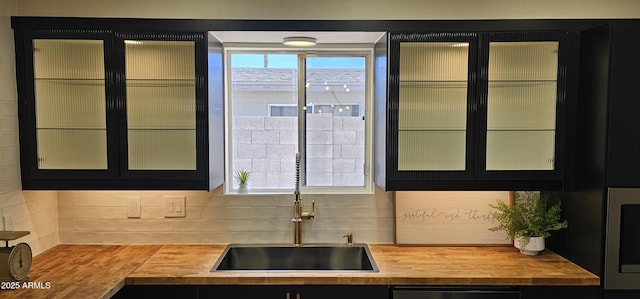 kitchen with butcher block countertops, a sink, black dishwasher, and dark cabinets