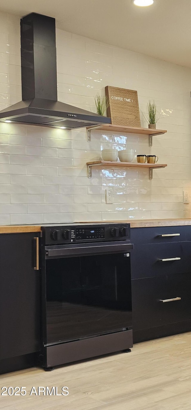 kitchen featuring black electric range oven, wall chimney range hood, backsplash, and light countertops
