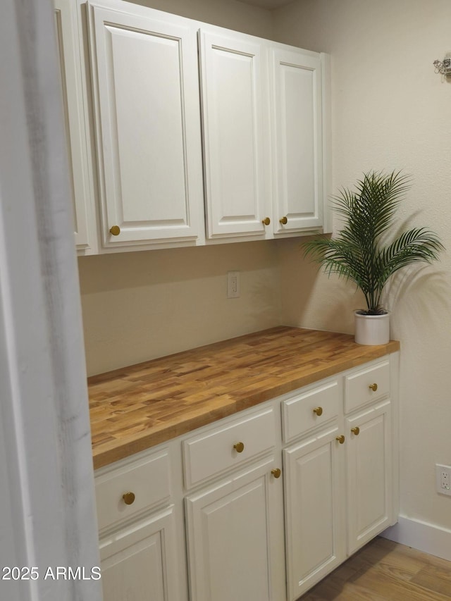 interior space featuring wooden counters, baseboards, white cabinetry, and wood finished floors