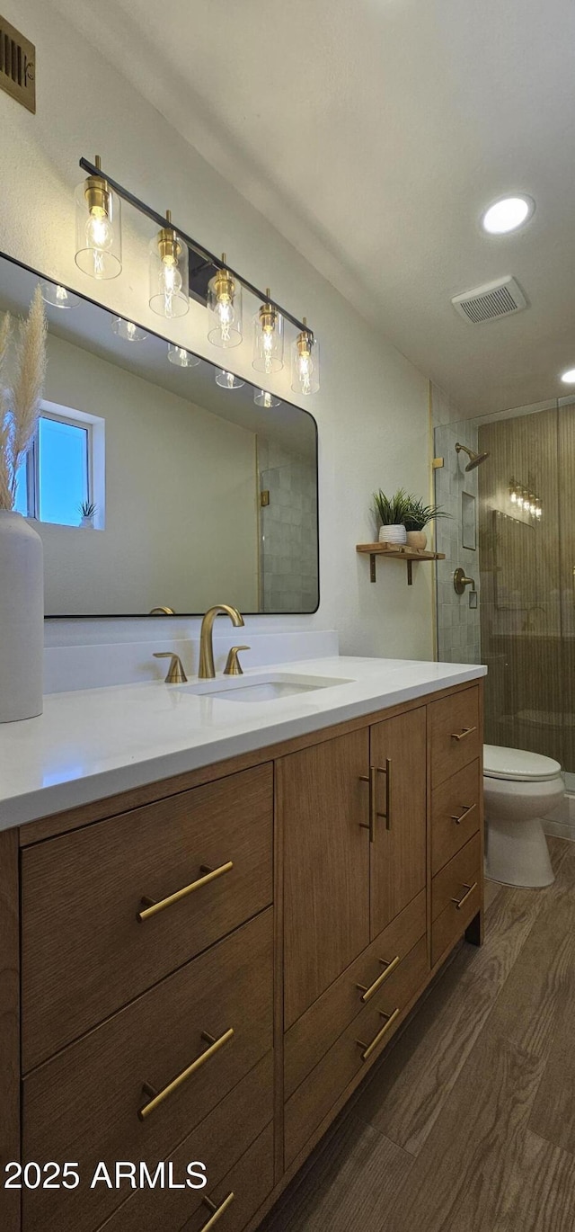 full bathroom with wood finished floors, vanity, a tile shower, and visible vents