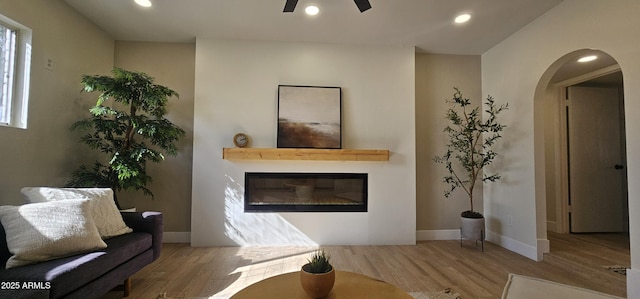 living area featuring wood finished floors, a glass covered fireplace, arched walkways, ceiling fan, and recessed lighting