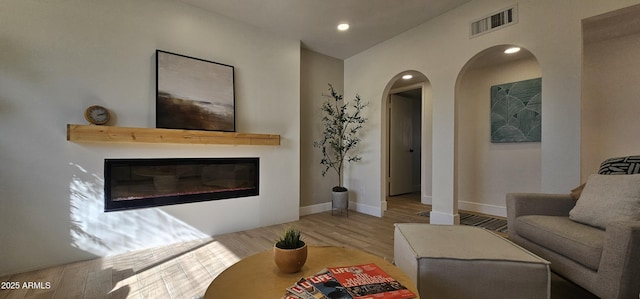 living room featuring baseboards, arched walkways, visible vents, a glass covered fireplace, and wood finished floors