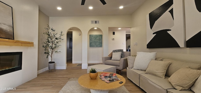 living room with a ceiling fan, light wood finished floors, baseboards, arched walkways, and recessed lighting