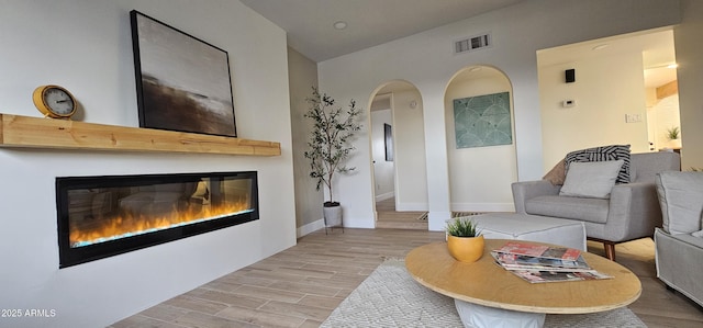 living room with visible vents, baseboards, wood finished floors, arched walkways, and a glass covered fireplace