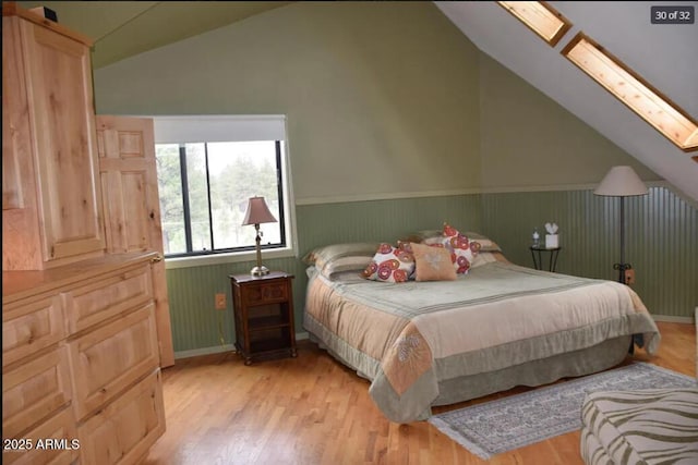 bedroom with lofted ceiling with skylight and light hardwood / wood-style flooring