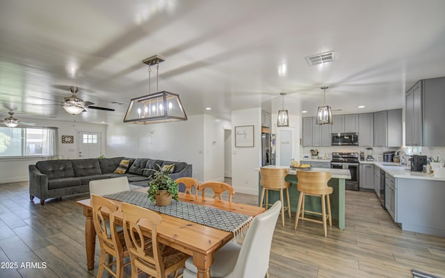 dining space with baseboards, visible vents, a ceiling fan, and light wood finished floors