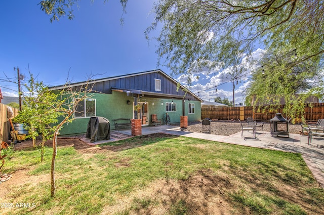 rear view of property featuring board and batten siding, a lawn, a fire pit, fence private yard, and a patio area
