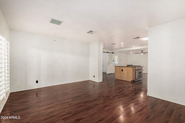 unfurnished living room featuring a wealth of natural light, ceiling fan, dark wood-type flooring, and a barn door