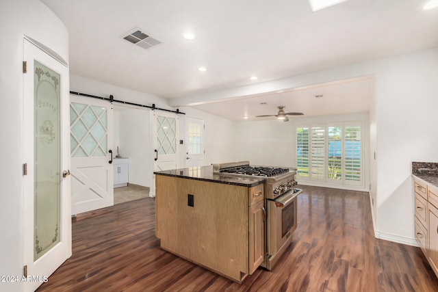 kitchen featuring dark wood-type flooring, a barn door, a kitchen island, ceiling fan, and stainless steel range