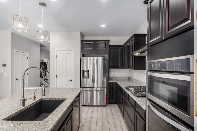 kitchen with stainless steel appliances, light wood-style flooring, a sink, light stone countertops, and exhaust hood