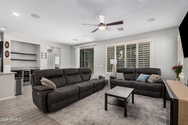 living room featuring light wood-style floors, beverage cooler, visible vents, and a ceiling fan