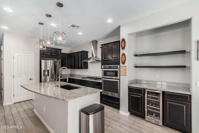 kitchen with wine cooler, visible vents, appliances with stainless steel finishes, a sink, and wall chimney exhaust hood