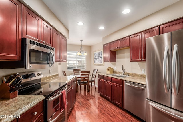 kitchen with dark wood-type flooring, sink, appliances with stainless steel finishes, decorative light fixtures, and a chandelier