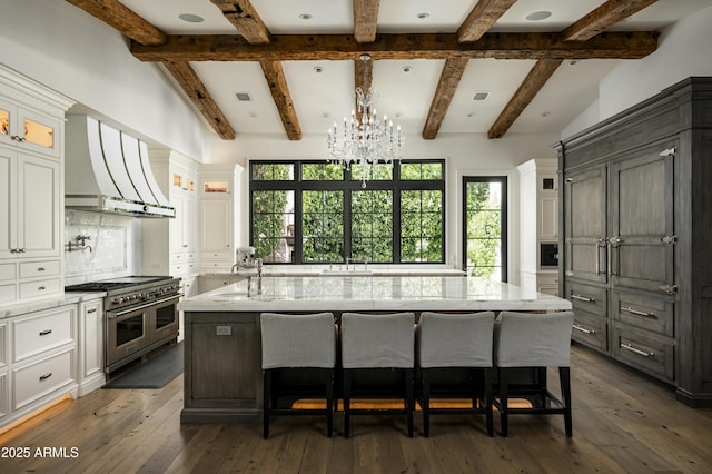 kitchen featuring a kitchen island with sink, double oven range, white cabinets, dark hardwood / wood-style flooring, and wall chimney exhaust hood