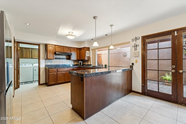 6208 E Paradise Ln, Scottsdale, AZ 85254 - kitchen featuring tasteful backsplash, a peninsula, decorative light fixtures, brown cabinets, and washer and dryer
